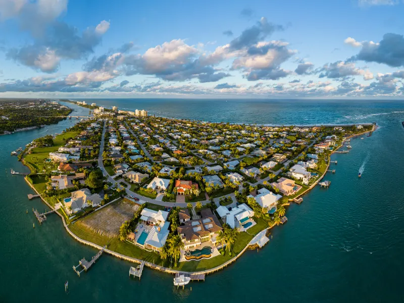 Aerial view of a coastal residential neighborhood surrounded by water on three sides under a partly cloudy sky.