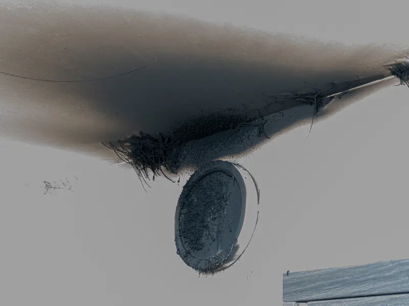 A wasp nest attached to the corner of a ceiling near a round light fixture.