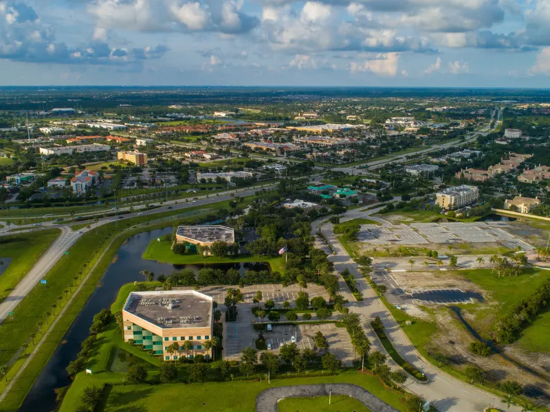 Aerial view of suburban office buildings, parking lots, roads, and green spaces under a partly cloudy sky.