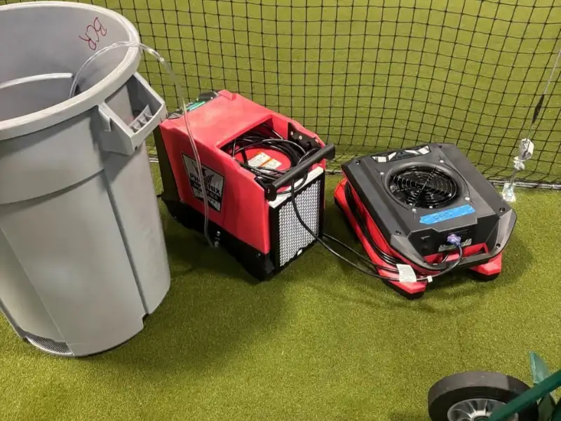 Red air scrubber and black fan unit connected to a gray trash bin on artificial turf.